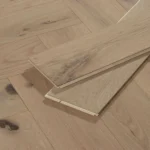 Two light oak floor planks resting on a herringbone patterned floor